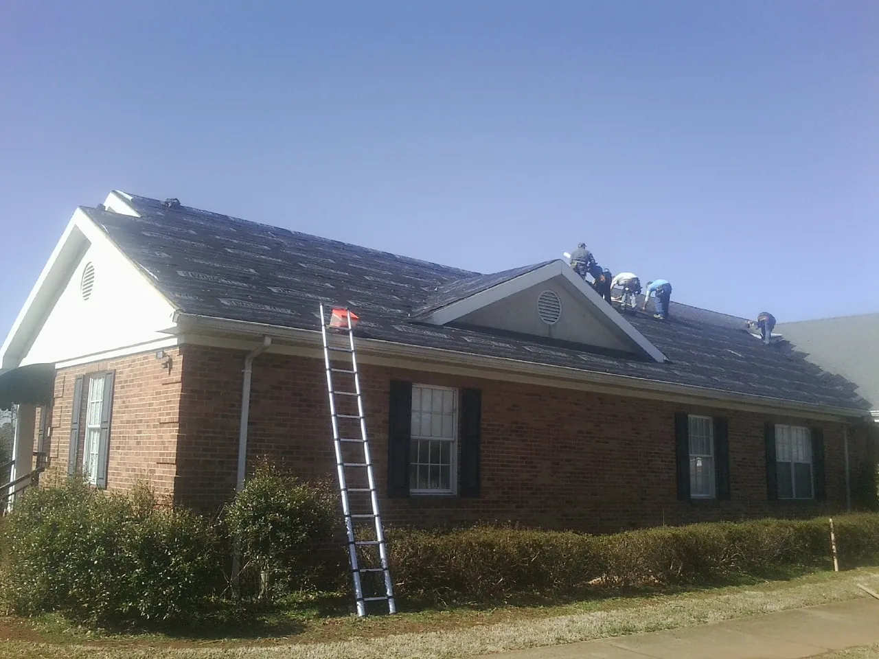Crew tearing shingles off a brick ranch roof with a ladder set — Emergency Roof Repair work by our crew in Lawrenceburg