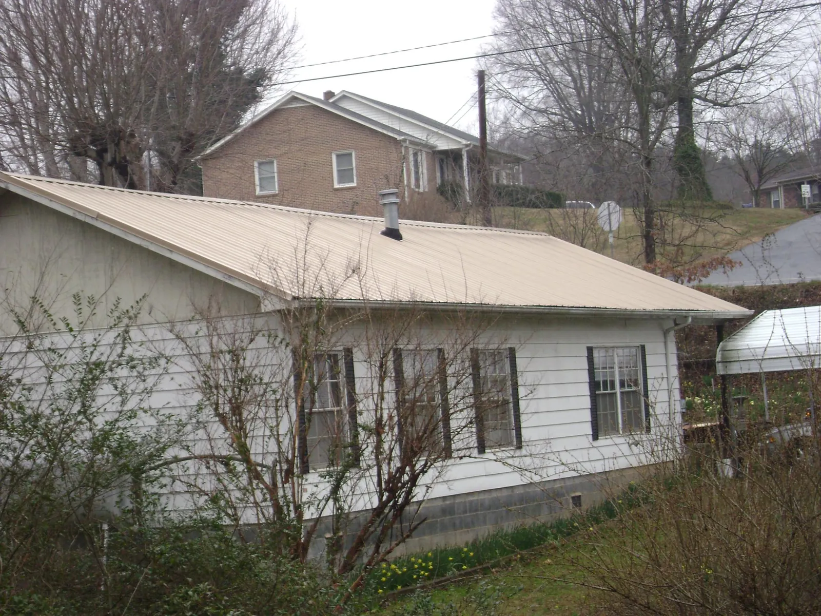 Tan metal roof on a white sided house set into a hillside — Commercial Roofing by Roofing Brothers in Lawrenceburg